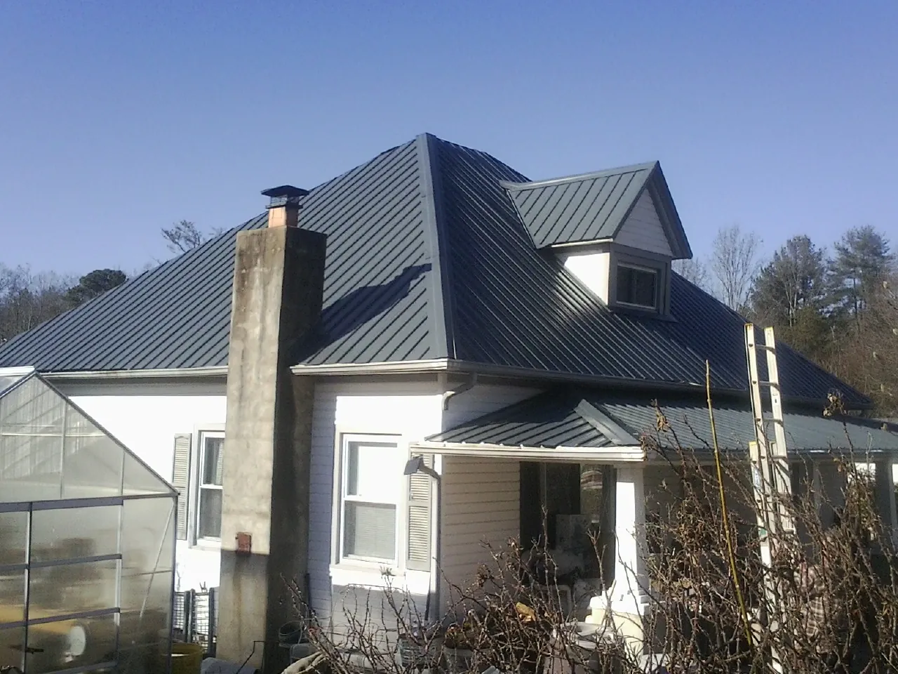 Dark blue standing seam metal roof on a white farmhouse with dormer — Slate & Tile Roof Repair by Roofing Brothers in Lindstrom
