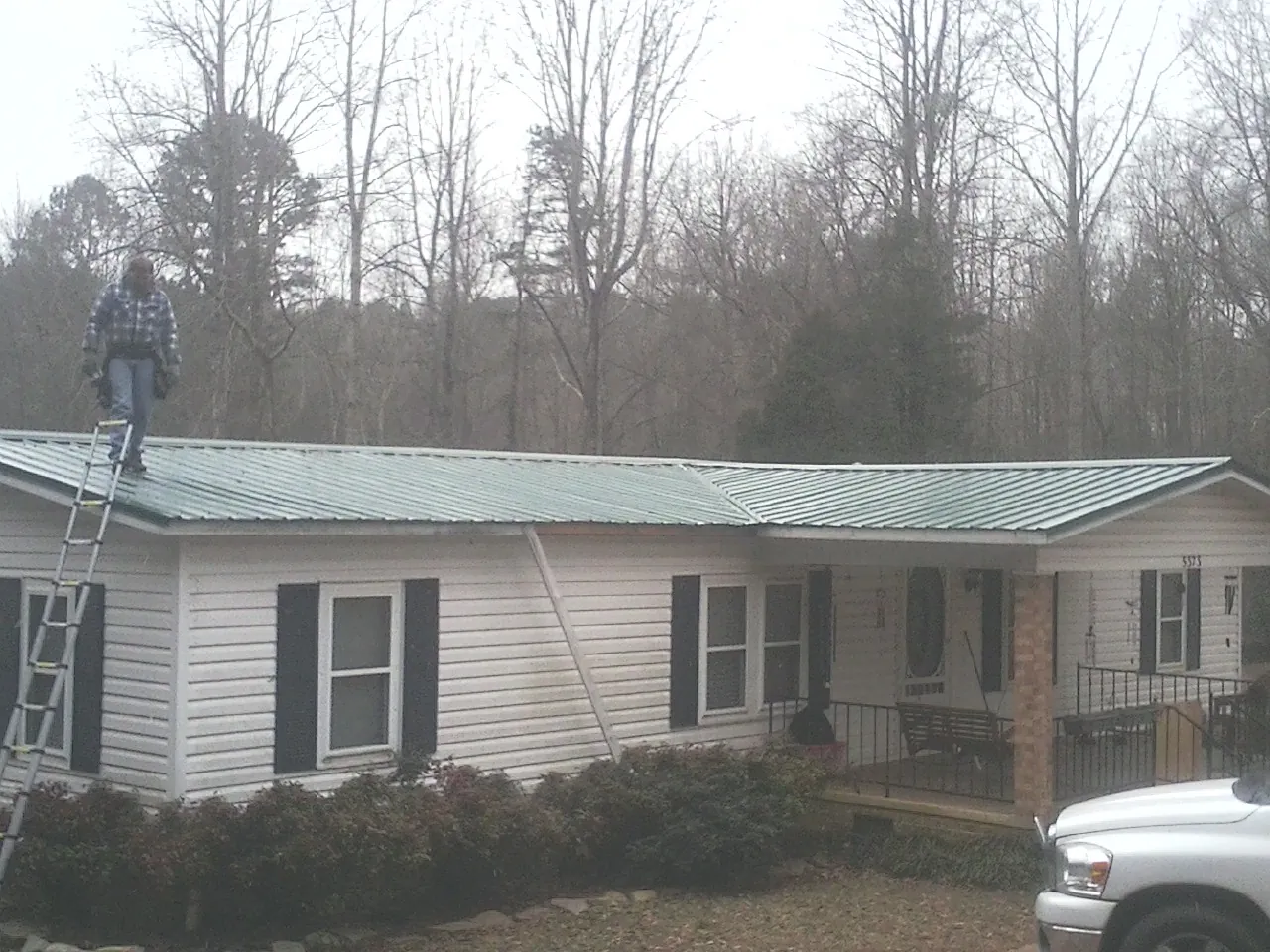 Worker on a ladder beside a new green metal roof on a ranch home in Lindstrom