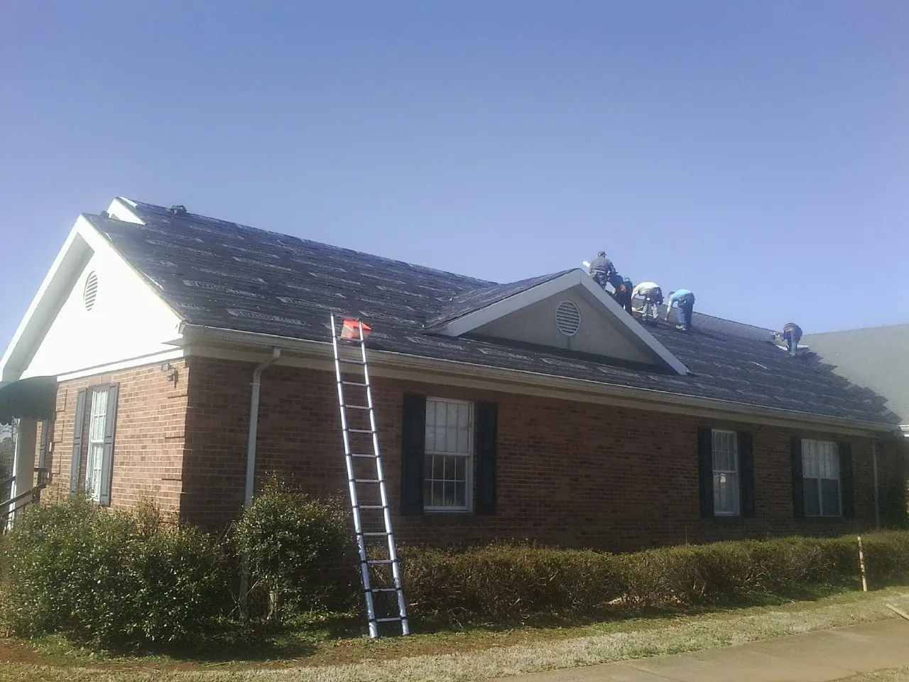 Crew tearing shingles off a brick ranch roof with a ladder set — Metal Roof Repair work by our crew in Lindstrom