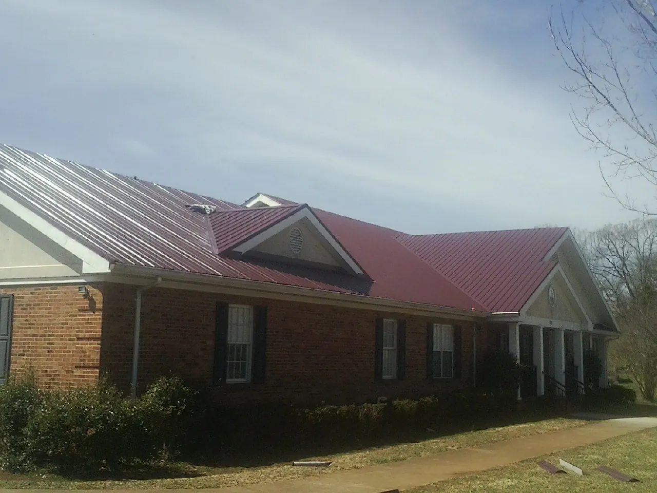Red metal roof with gabled entries on a long brick building, from a Hail Damage Roof Repair job in Lindstrom