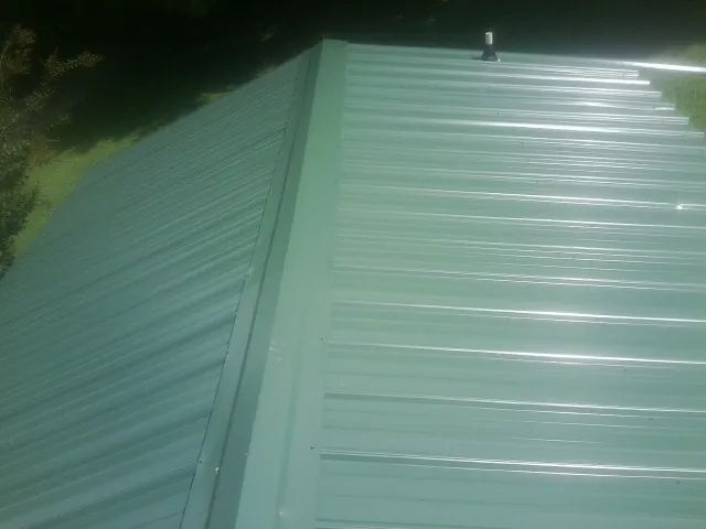 New green metal panels meeting at the ridge of a roof — Flat Roof Repair work by our crew in Lindstrom