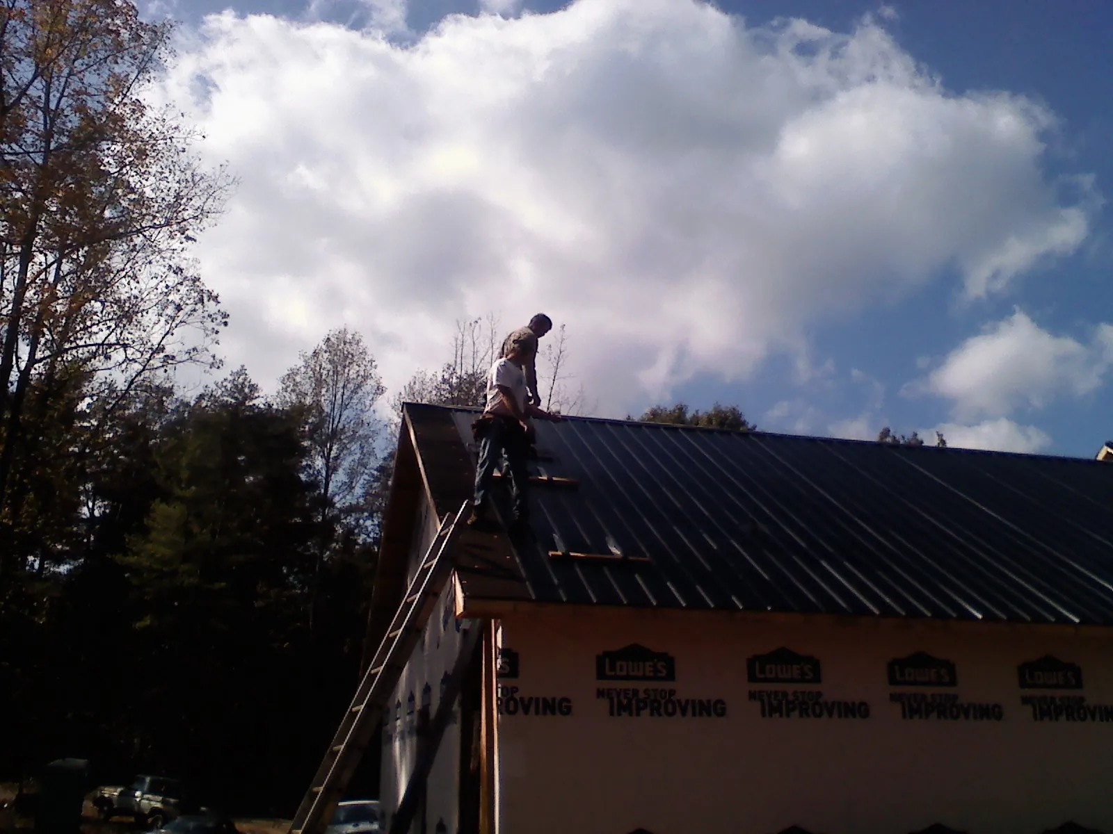 Roofer fastening dark metal panels high against a cloudy sky, from a Roof Inspection job in Lindstrom